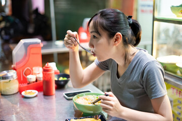 Enjoying a delicious bowl of noodles at a lively street food stall in an Asian city during the...
