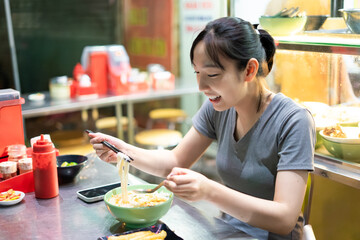 Enjoying delicious noodles at a bustling street food stall in a vibrant Asian city during the...