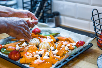 Senior Male Hands Sprinkling Feta Cheese Over Roasted Vegetables in a Modern Kitchen