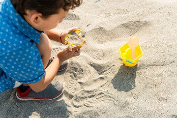 Child playing with sand mold on beach creating summer memories
