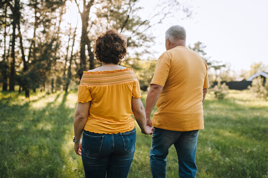 Elderly gray-haired man and adult woman walking holding hands in the forest on green grass outdoors. Photography, portrait.