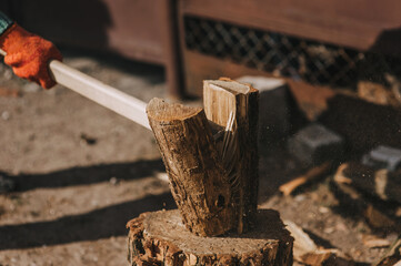 Adult male pensioner strong lumberjack in gloves chopping log on stump with axe in forest at sawmill in rural area outdoors. Close-up photo, portrait.