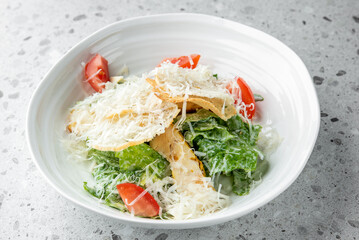 Fresh Caesar salad with crispy croutons, grated Parmesan cheese, and sliced tomatoes in a white bowl on a speckled gray countertop, capturing a gourmet and healthy dining experience