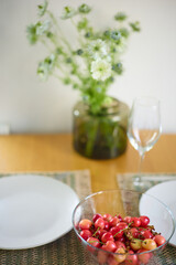 a bouquet of daisies in a glass vase stands on a table on a white background, a wine glass, a wine glass, plate with ripe cherries, table setting, plates, defocus, macrophotography, bokeh