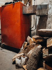 An old, large, red wood-burning central heating stove, with a supply of cut firewood logs next to it
