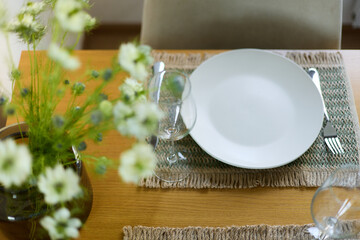 a bouquet of daisies in a glass vase stands on a table on a white background, a wine glass, table setting, plates, defocus, macrophotography, bokeh