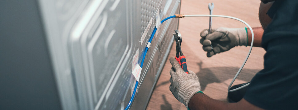 Panorama view male technician wearing knit gloves connecting copper water line behind brand new fridges on vinyl floor, install water line for new refrigerator. Hands during appliance setup