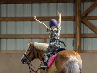 boy riding horse excitedly with arms in air