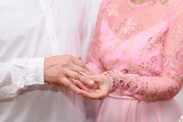 Bride's manicured fingers gently slide gold wedding band onto groom's finger.Bride's delicate hand...