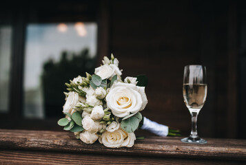 Photo of a wedding bouquet of roses from the bride and a glass of champagne.