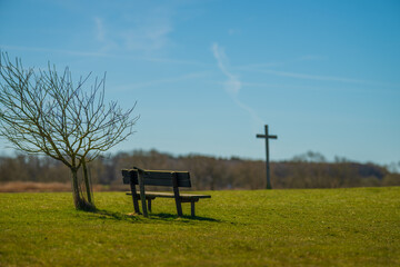 Bench and tree beside wooden cross on grassy field.