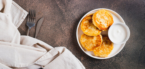 Appetizing potato fritters and sour cream on a plate on the table top view web banner