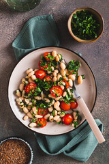 Vegetarian white bean, tomato and herb salad on a plate on the table top and vertical view