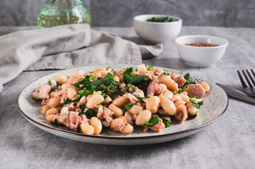 Appetizing salad with tuna, white beans and greens on a plate on the table