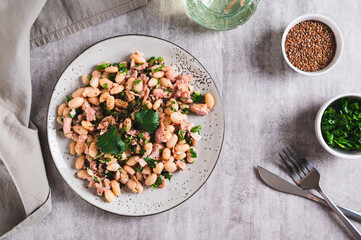 Appetizing salad with tuna, white beans and greens on a plate on the table top view