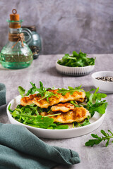 Warm salad with grilled halloumi and arugula on a plate on the table vertical view