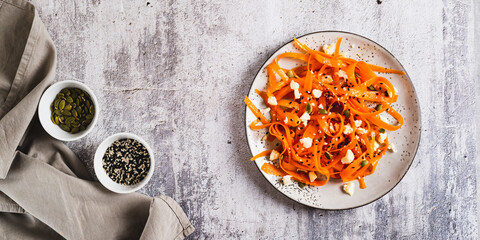 Homemade carrot slices in spices with ricotta and pumpkin seeds on a plate top view web banner
