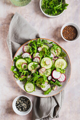 Cucumber, radish and greens salad mix on a plate on the table top and vertical view