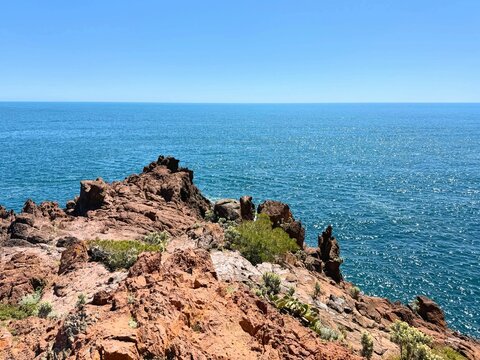 Dramatic red coastal rocks with vibrant blue sea under a clear sky in the Calanques de l'Estérel region near Saint-Raphaël, France. - Powered by Adobe