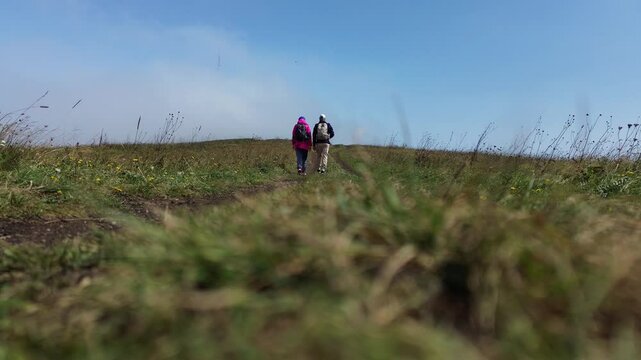  Two Backpackers - Haikers Walking Away on a Dirt Road, Ground-Level Shot, Rear View, Against a Blue Sky