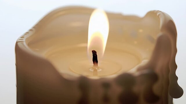 Close Up of a Burning Cream Colored Wax Candle with Dripping Wax on White