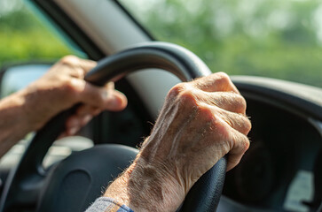 Hands of an elderly father driving a car during a family road trip across Russia. Close-up shows details of aging skin, veins, and sunlight on arm hair