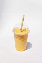Plastic glass of creamy lucuma smoothie with a paper straw on white background. Healthy drink. Take away food.