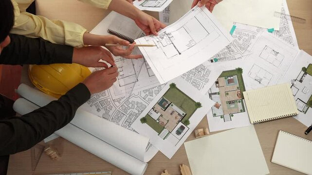 Architect and safety engineer discussion about building construction use blueprint on table with architectural document, measurement tool and wooden block scatter around at modern office. Delineation.