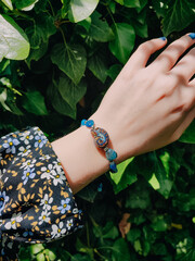 Blue stones kyanite aquamarine apatite beaded bracelet on woman's wrist. Green leaves background,...