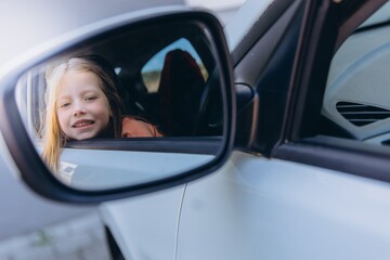 A 6-year-old girl sitting in the driver seat of in car playfully looks into the rearview mirror. Childhood curiosity and imagination in a vintage car setting