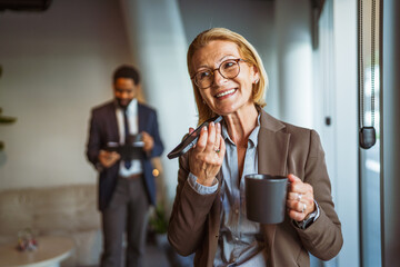 Mature businesswoman leaving voice message and drink coffee in office