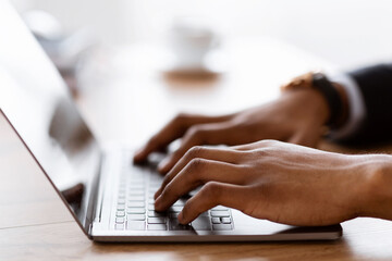 Selective focus on male hands typing on laptop keyboard, cropped, side view. African american businessman sending emails to clients or assistant. Modern technologies and business concept