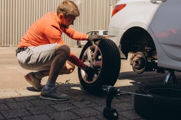 Man changing car tire on roadside using tools, vehicle lifted on jack. Concept of auto repair,...
