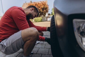 Man changing car tire on roadside using tools, vehicle lifted on jack. Concept of auto repair,...