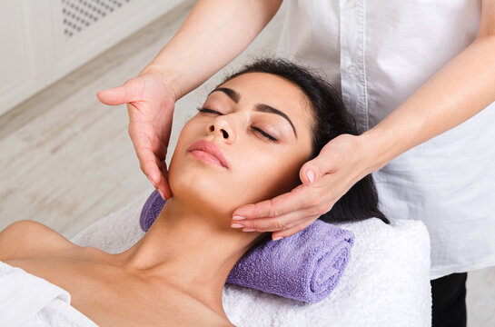 Neck massage in spa. Female beautician work in wellness center. Professional massagist make relax healthy procedure to beautiful indian girl in cosmetology cabinet or beauty parlor.