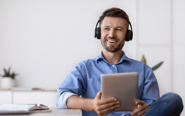 Handsome Millennial Freelancer Guy In Wireless Headphones Relaxing With Digital Tablet At Home...