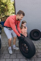 Close-up of a man changing a car tire in front of his house. The vehicle is lifted with a jack,...