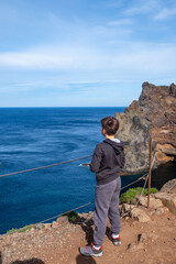 Young boy stands on volcanic cliff edge Madeira island, hiking adventure, cliffside trail, gazing...