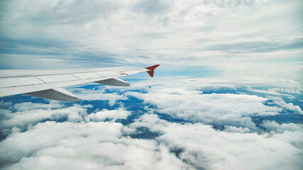 Airplane wing cutting through misty clouds, revealing expansive landscape during flight