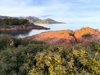 Golden hour light over the red rocky coastline of the C&ocirc;te d&rsquo;Azur, France, with the Esterel mountains in the background and calm Mediterranean waters.  
