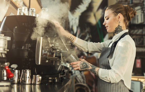 Fototapeta Happy young tattooed barista making coffee in professional coffee machine. Woman preparing beverage. Small business and professional coffee brewing concept