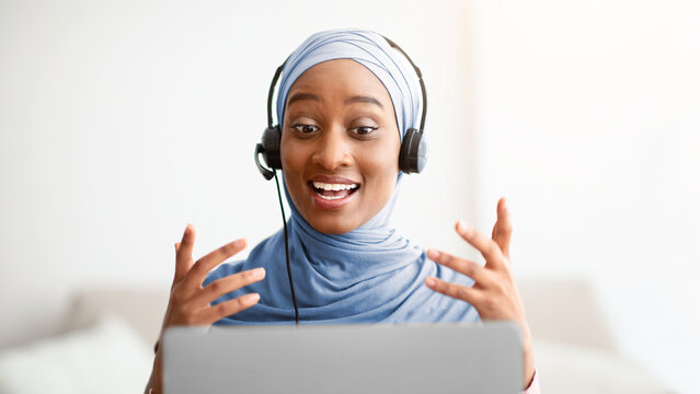 Remote work, communication, education. Happy Muslim lady in hijab wearing headset, having video call on laptop at home. Young Arab woman talking on web at home, taking part in business web conference