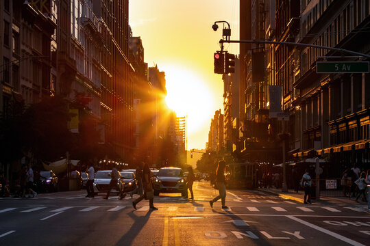 Crowded intersection with busy people and traffic on 5th Avenue in New York City with sunset light shining in the background