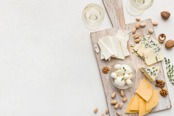 Set of cheese with nuts on wooden board and wine glasses over white concrete background, top view,...