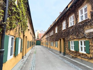Historic alley in the Fuggerei, the world’s oldest social housing complex, located in Augsburg, Germany, with colorful facades and green shutters.