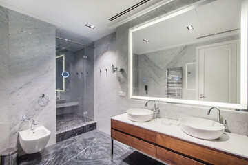 The bathroom is decorated with gray marble tiles, with a glass door to the shower and a .large...