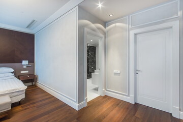 Bedroom with light walls, brown laminate flooring and a white door to the bathroom.