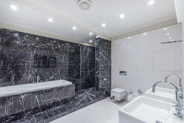 Luxurious bathroom with white and black tiles. A large bathtub and a glass door to the shower.