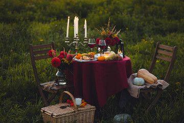 Fall mood, romantic date outdoors in the garden, candlelight dinner for a couple. Private wedding for two. Pumpkin countryside decor, red dahlia, cheese plate, grapes. Gourmet food, elegant setting 