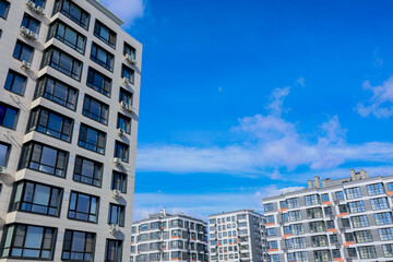 Multi-storey residential buildings of modern architecture with large windows and balconies against the background of the sky and clouds. The concept of residential complexes, urban life, residential